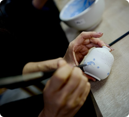 Gros plan sur des mains peignant un petit vase en argile blanche