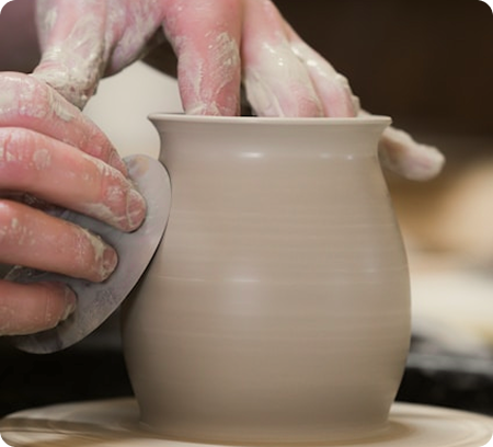Mains d'un élève peaufinant un pot cru sur un tour de potier avec un outil