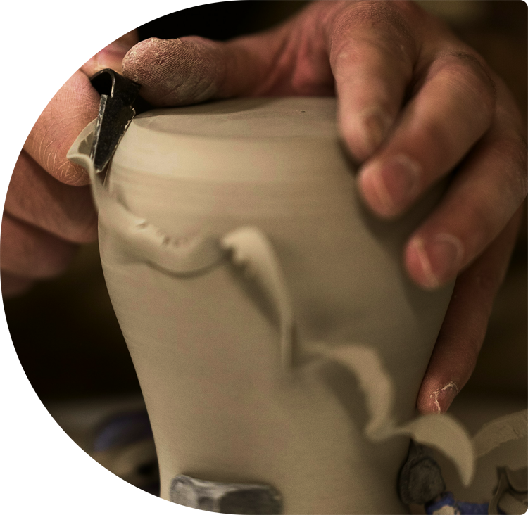 Photo des mains d'un adulte façonnant un pot en argile avec un outil